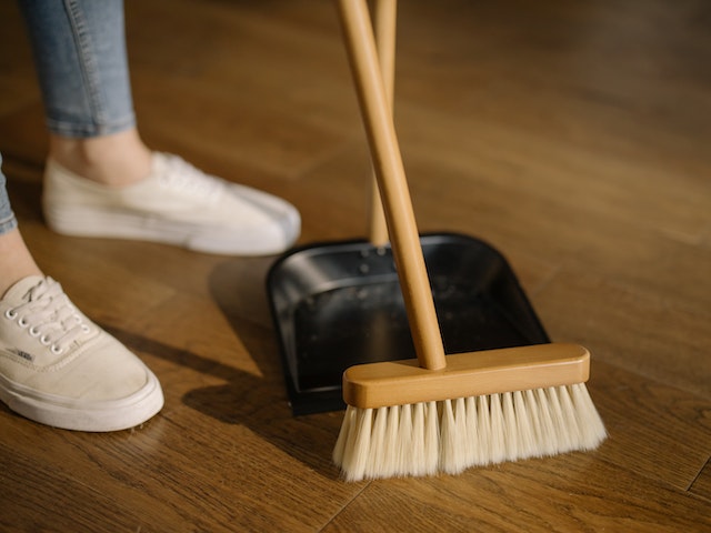 Person wearing white pants and white socks standing besides brown broom